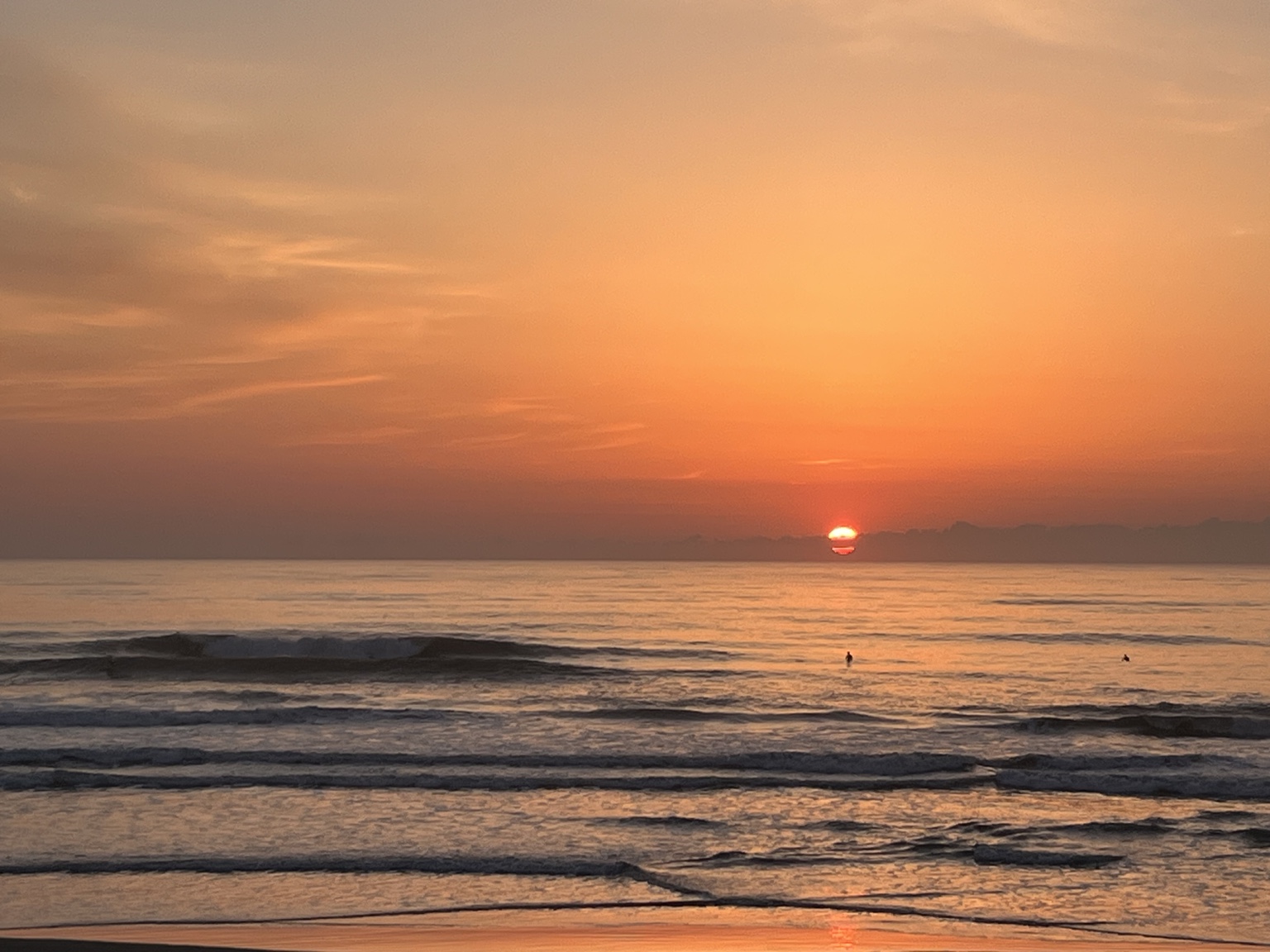Surfers beneath an orange sunrise at Ichinomiya